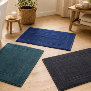 Trois tapis de bain en coton bleu, lagon et noir posés sur un sol en bois clair